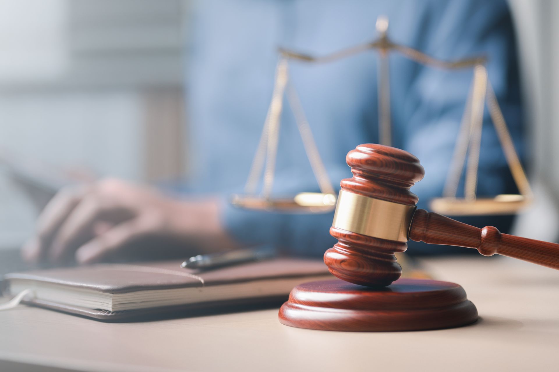 Marteau de juge sur un bureau, avec une balance de justice et une personne floue en arrière-plan.