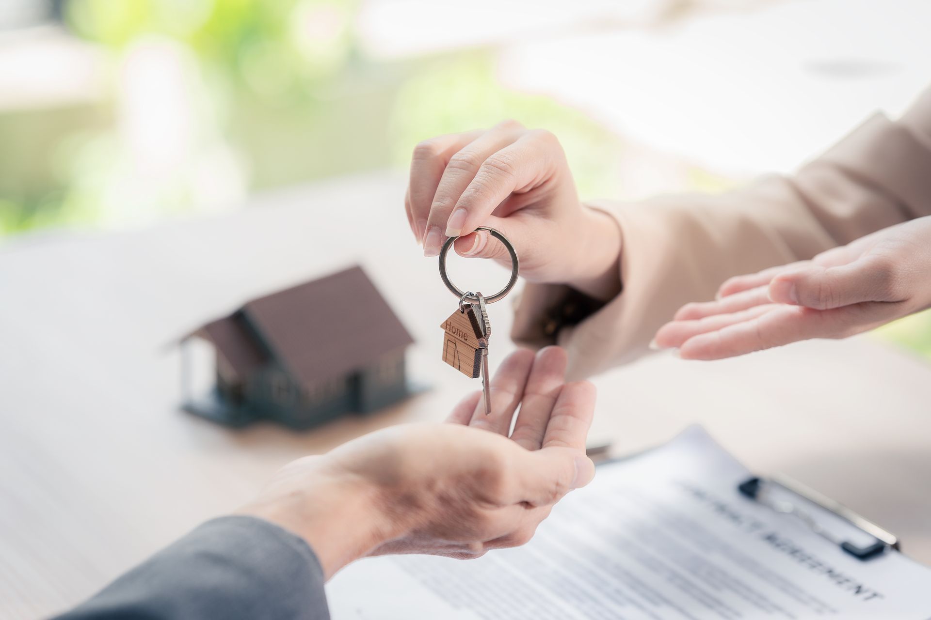 Des mains s’échangeant les clés d’une maison au-dessus d’un contrat, dans un bureau lumineux
