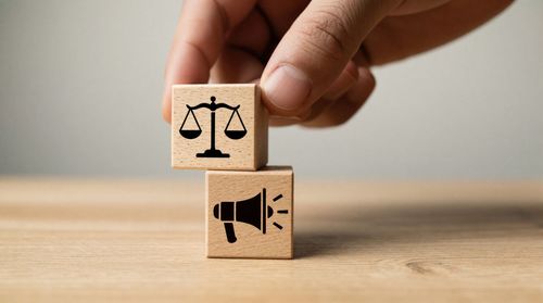 Empiler deux blocs de bois à la main, l'un avec une icône de balance et l'autre avec une icône de mégaphone.