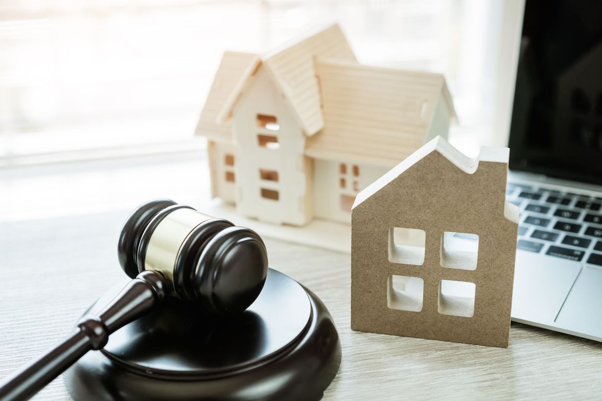 Un marteau de juge à côté de maquettes de maisons sur un ordinateur portable, évoquant le droit immobilier.