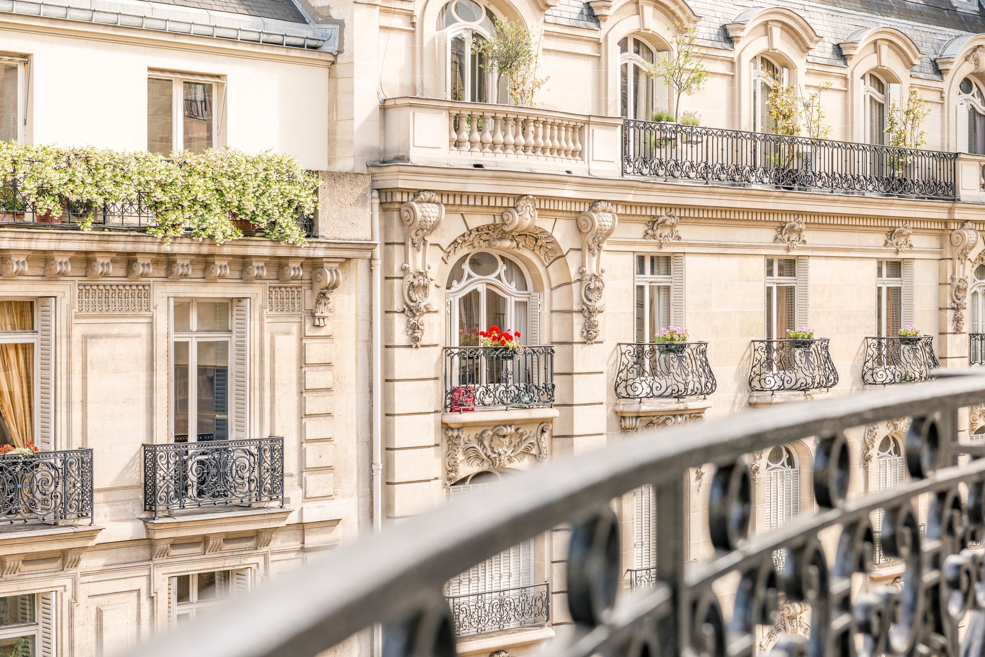 Élégants immeubles parisiens couleur crème, dotés de balcons en fer forgé, vus depuis une rambarde de balcon.