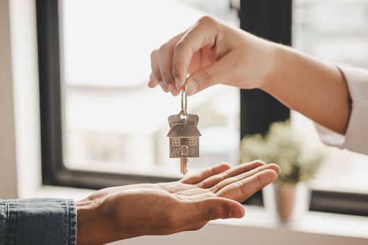 Une main tendant les clés de la maison à une autre main tendue près d'une fenêtre.