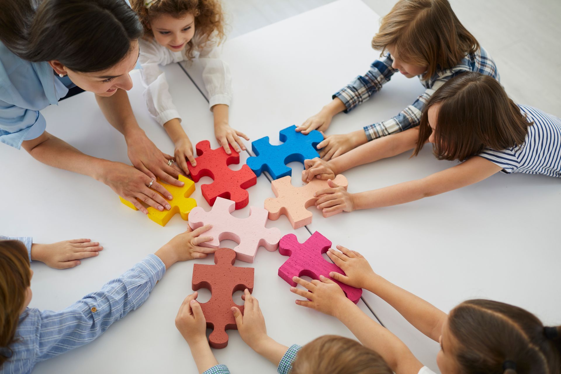 Des personnes tendent les bras pour assembler des pièces de puzzle colorées sur une table.