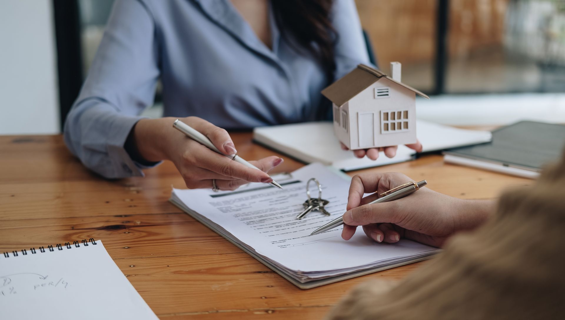 Deux personnes examinent une maquette de maison et des plans au sol autour d’une table en bois.