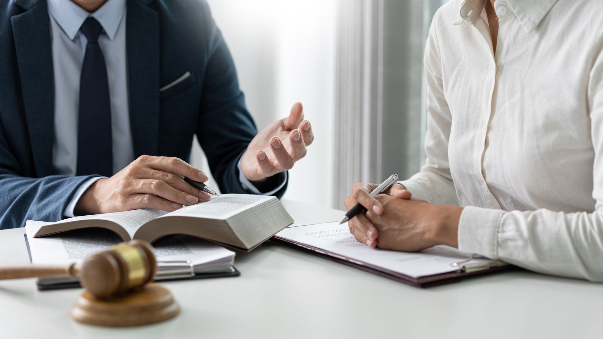 Un avocat et son client discutent de documents à un bureau, avec un marteau de juge au premier plan.