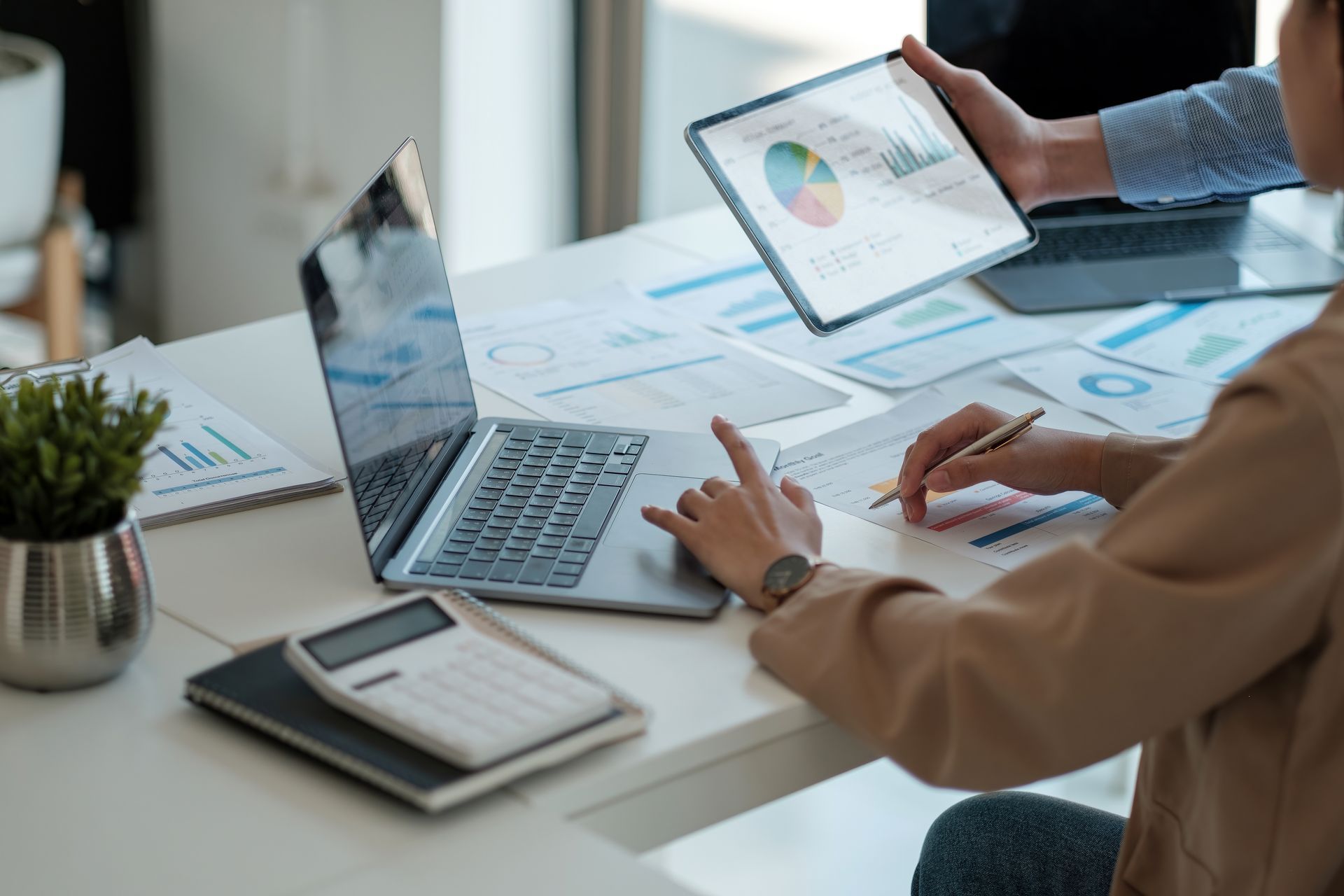 Deux personnes consultent des graphiques sur un ordinateur portable et une tablette à un bureau dans un bureau lumineux.