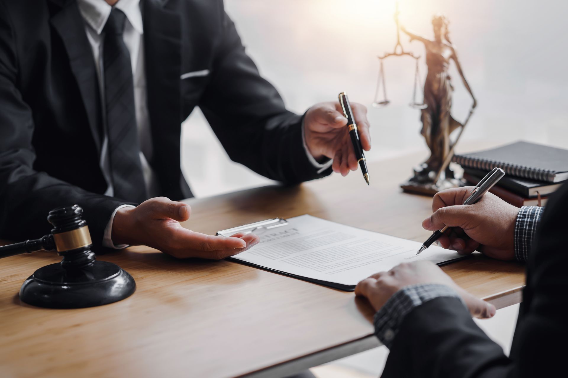 Des avocats examinent un contrat à un bureau, avec un maillet et une balance de justice à proximité.
