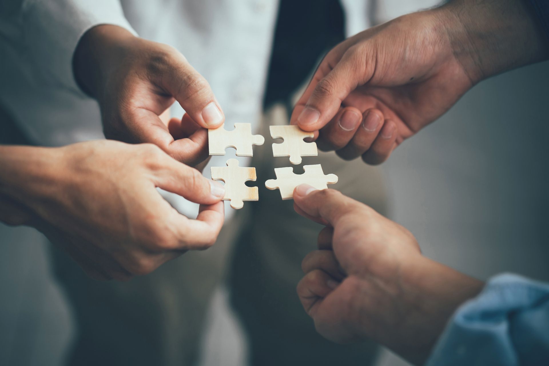 Des mains assemblant des pièces de puzzle blanches.