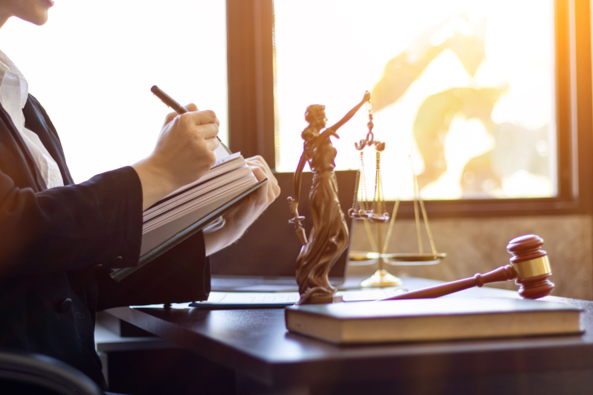 Un avocat prend des notes à côté d’une statue de la Justice et d’un marteau de juge, dans un bureau ensoleillé