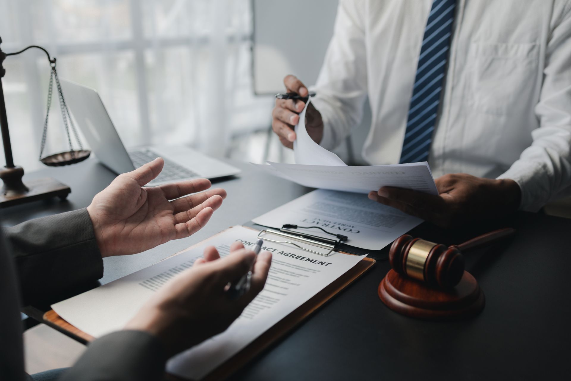 Un avocat s’entretient avec un client à un bureau, entouré de documents juridiques, d’une balance de justice et d’un maillet de juge