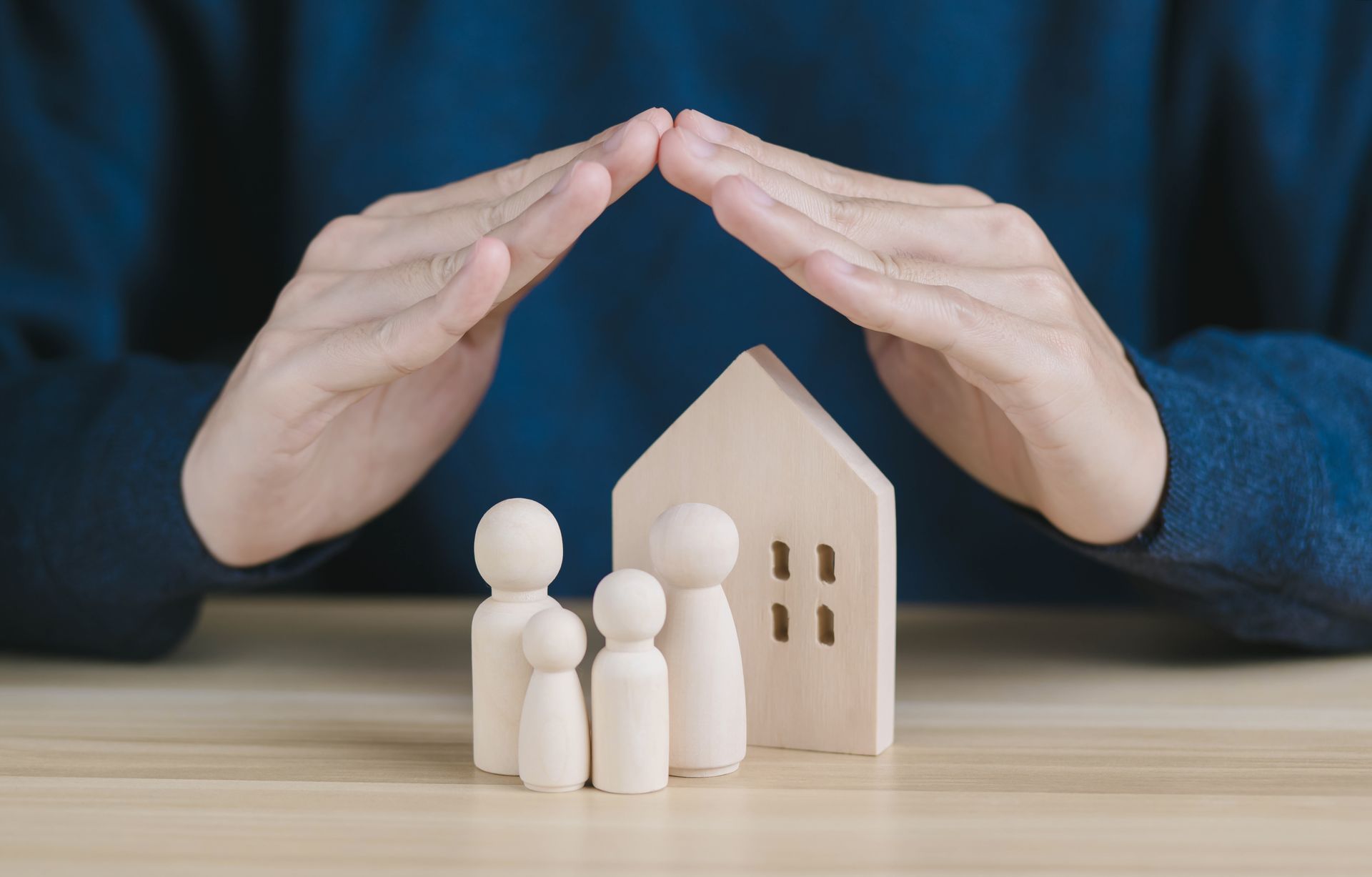 Des mains protégeant une maquette de petite maison et des figurines.