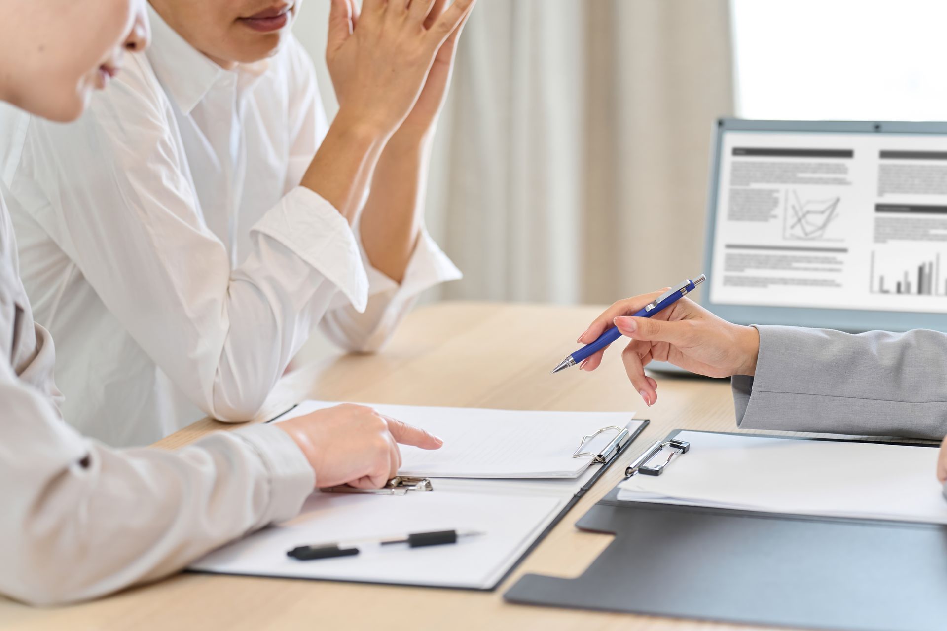 Réunion d’affaires avec des personnes examinant des documents autour d’un bureau, un ordinateur portable affichant des graphiques et des diagrammes