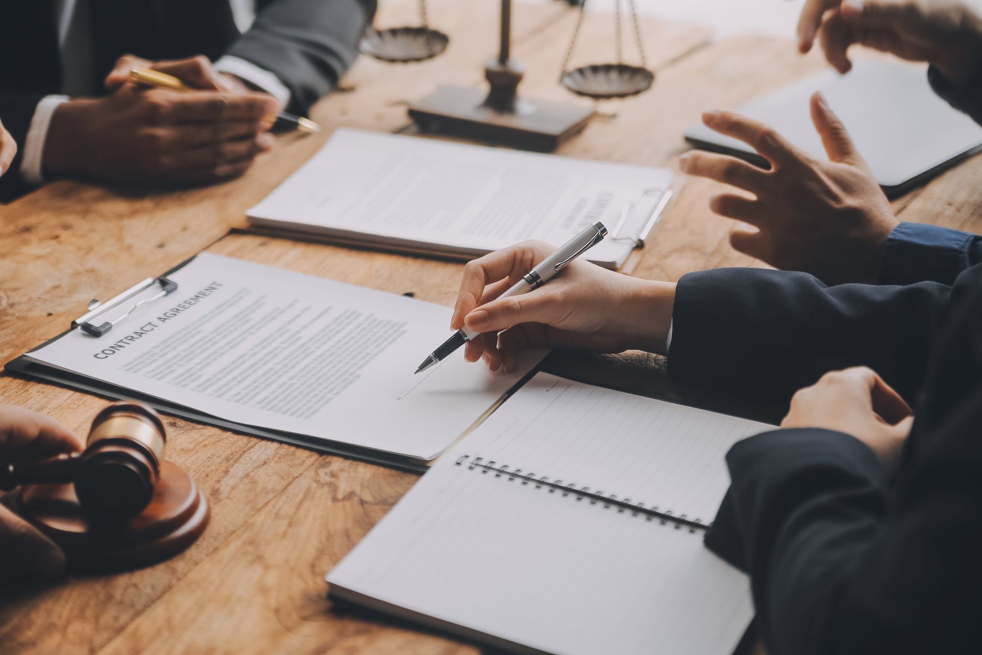 Des personnes en réunion d’affaires signent des documents autour d’une table en bois, avec du café et une balance de la justice.