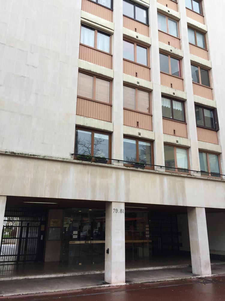 Extérieur d'un immeuble d'appartements beige avec balcons et entrée couverte au rez-de-chaussée.