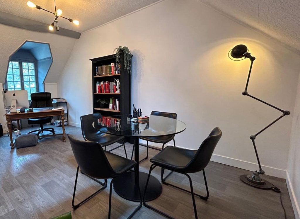 Bureau à domicile moderne avec bureau noir, étagères, chaises et lampadaire à bras long sous un plafond mansardé.