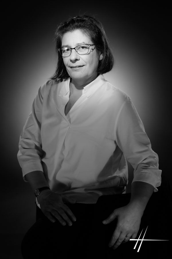 Portrait en noir et blanc, réalisé en studio, d'une personne assise portant des lunettes et une chemise claire, arborant un doux sourire.
