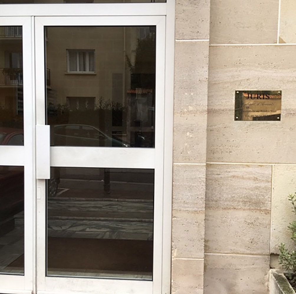 Porte d'entrée vitrée jouxtant un mur en pierre beige avec une petite plaque fixée à droite.