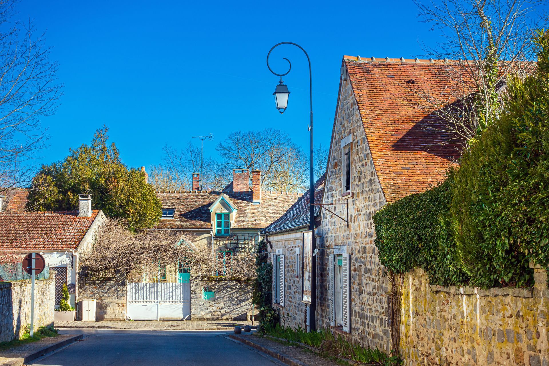 Rue de village tranquille bordée de maisons en pierre aux toits de tuiles rouges, sous un ciel bleu.