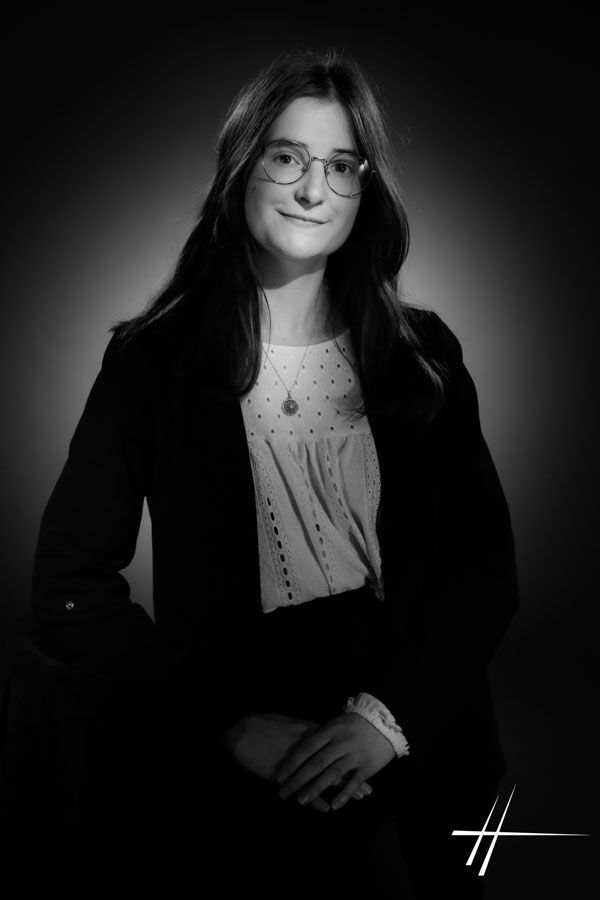 Portrait en noir et blanc d'une femme à lunettes, souriant doucement sur fond sombre.