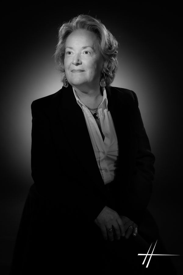 Portrait en noir et blanc, réalisé en studio, d'une personne en costume sombre, assise et regardant sur le côté.