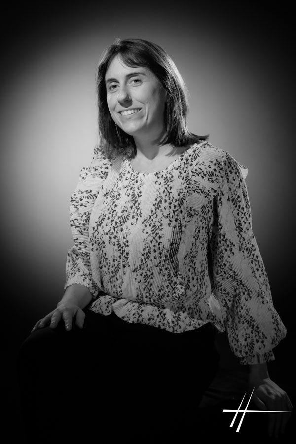 Portrait en noir et blanc d'une personne souriante assise sur un fond sombre uni.