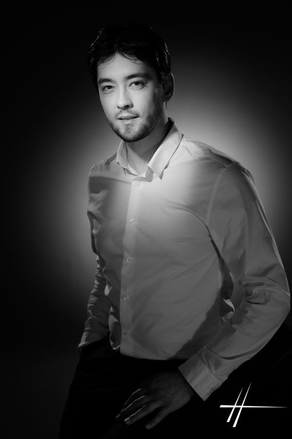 Portrait en studio, en noir et blanc, d'une personne en chemise boutonnée, se détachant sur un fond sombre.