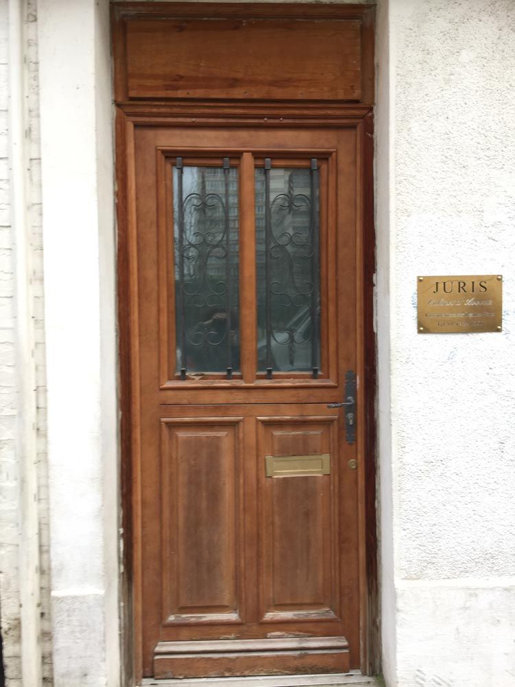 Porte d'entrée en bois avec vitres et plaque en laiton sur un mur blanc.