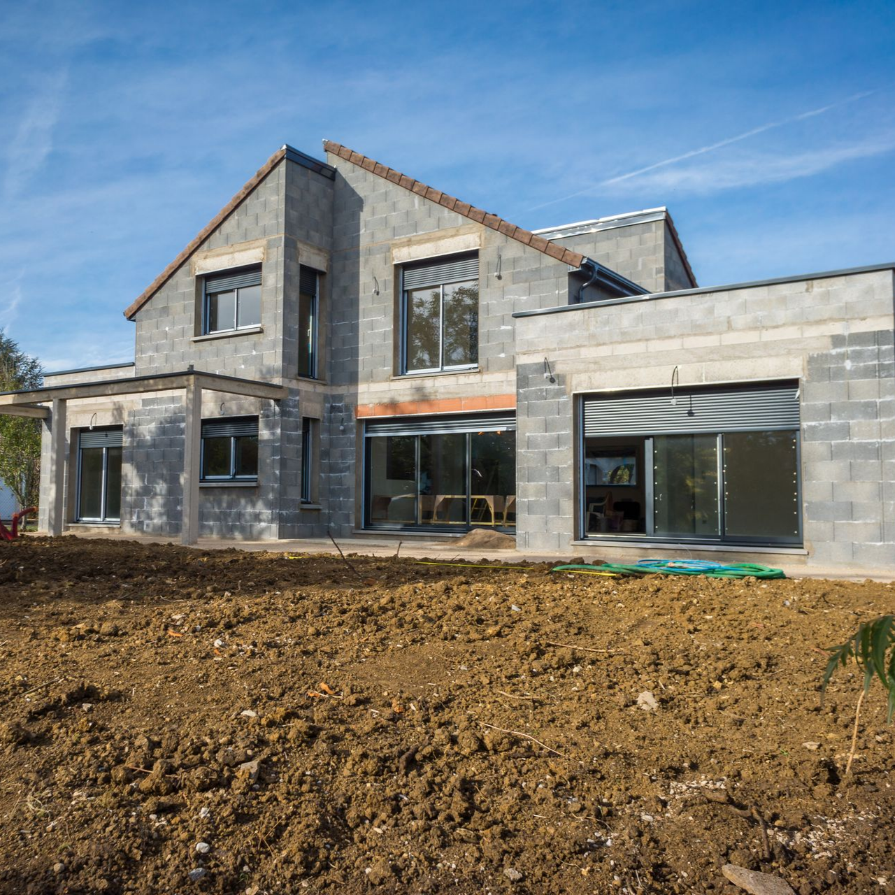 Une maison moderne en béton de deux étages en construction, avec de grandes portes et fenêtres.