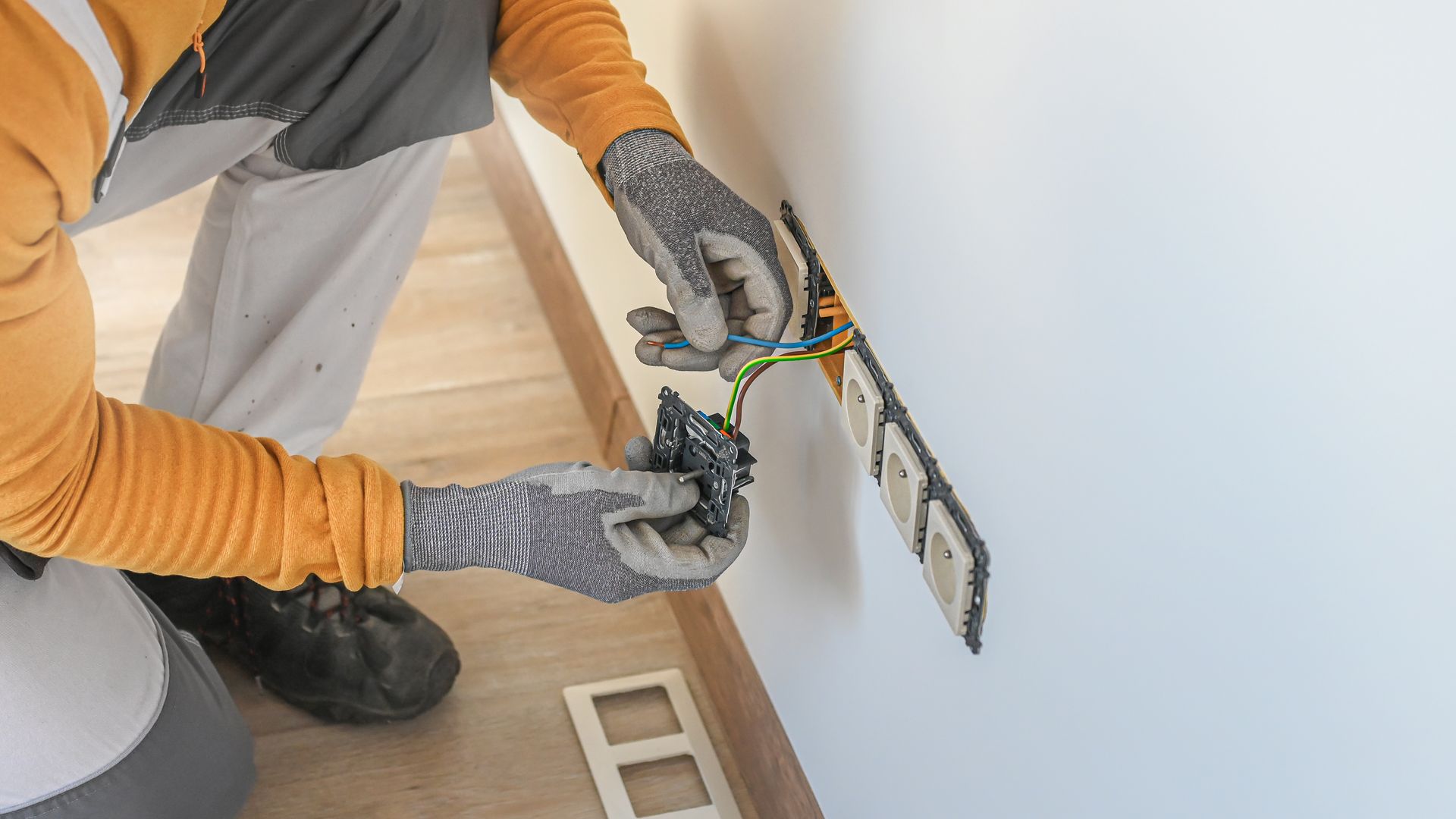 Un électricien vêtu d'une chemise jaune et de gants de protection installe un câble pour une prise électrique.