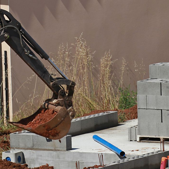 Un godet d'excavatrice contenant de la terre rouge surplombe un chantier de construction.