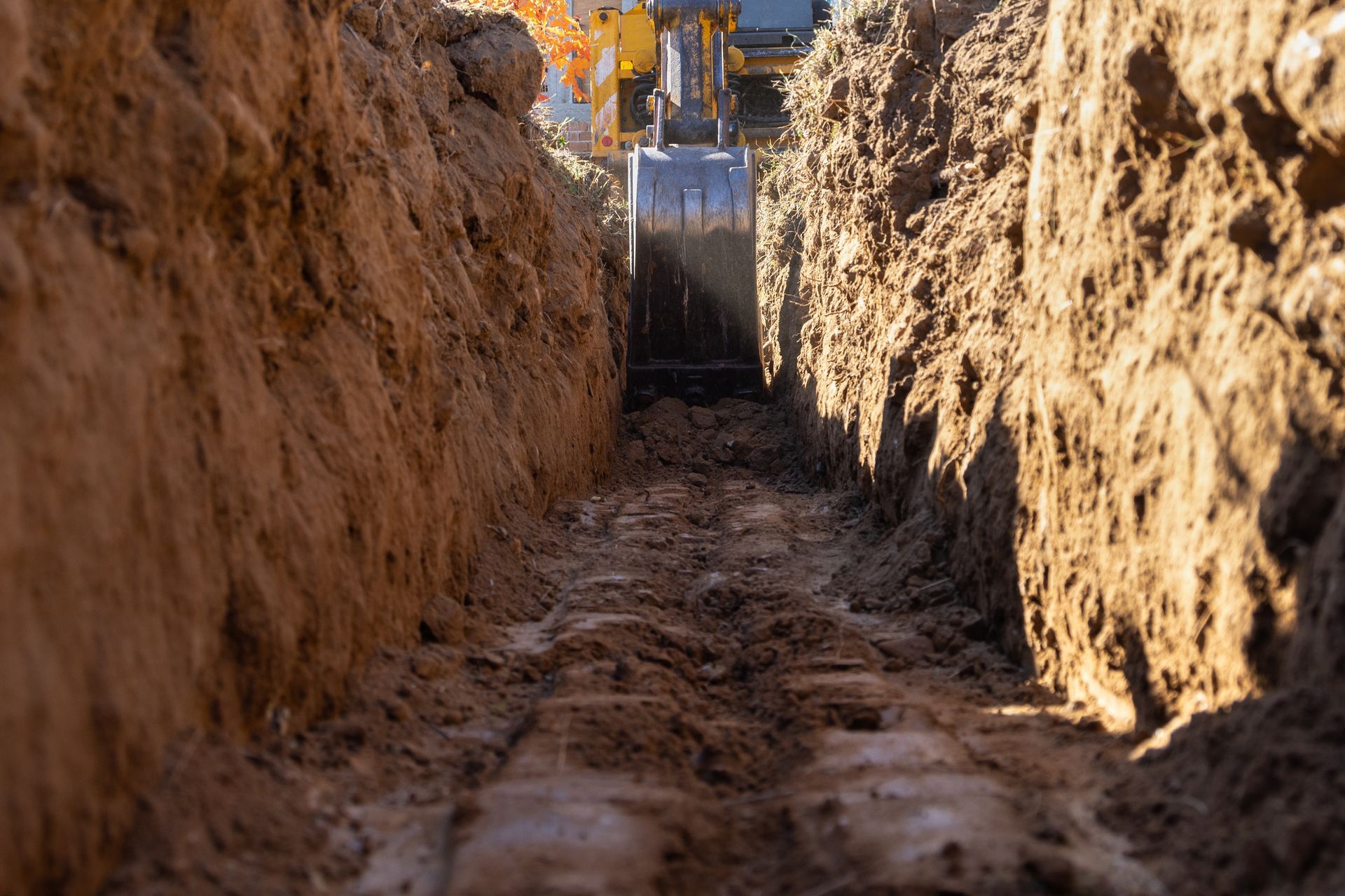 Le godet d'une excavatrice de chantier creuse une tranchée étroite et profonde dans un sol brun.