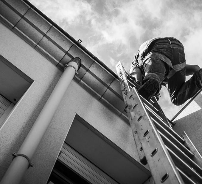 Ouvrier grimpant à une échelle le long du toit d'un bâtiment, vu d'en bas en noir et blanc