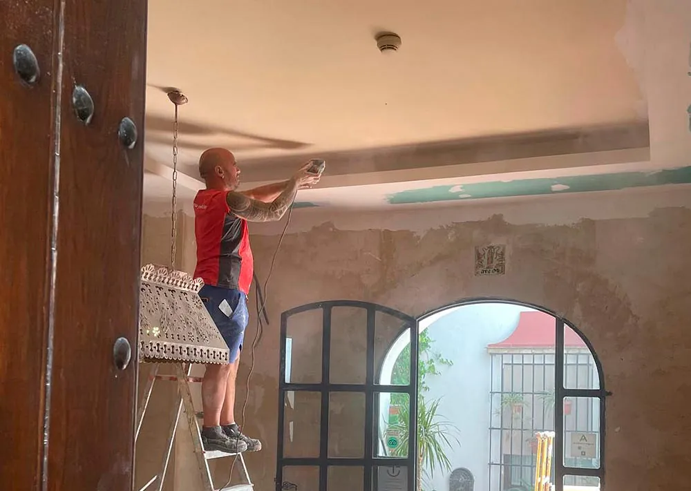 Un hombre está de pie en una escalera pintando un techo.