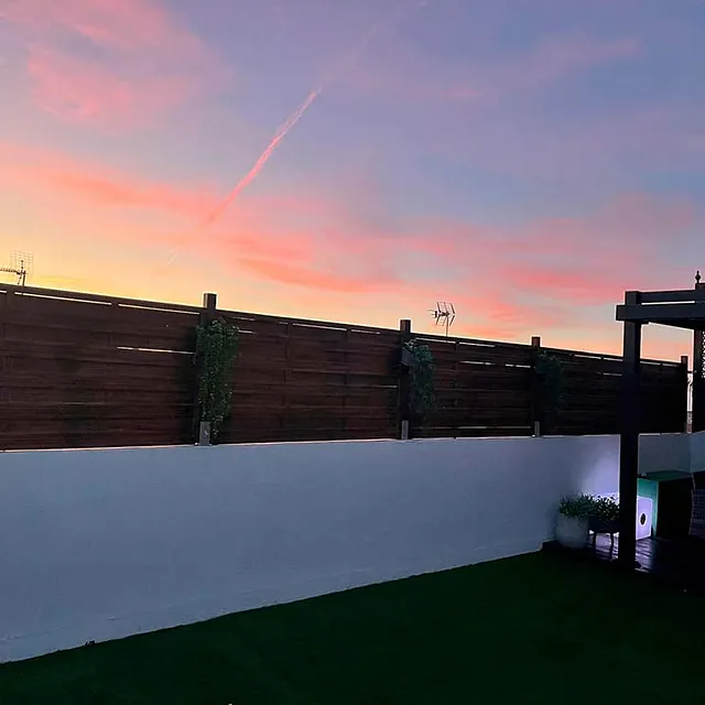 Una valla de madera rodea un exuberante patio verde al atardecer.