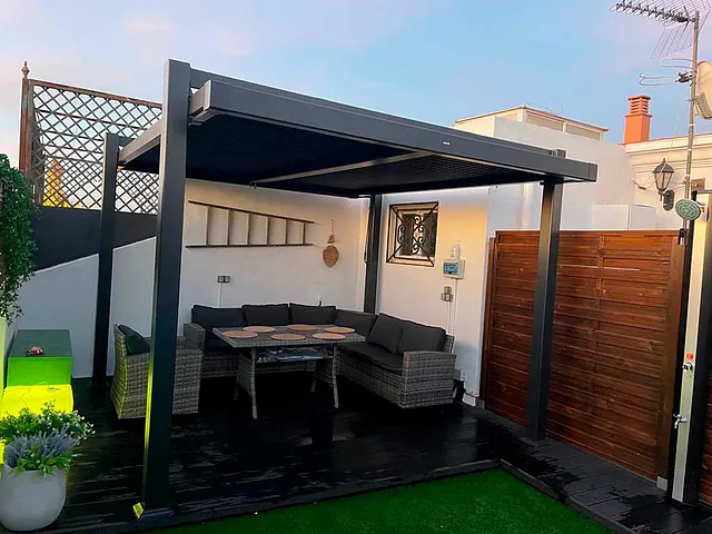 Un patio con sofá, mesa y sillas bajo una pérgola.