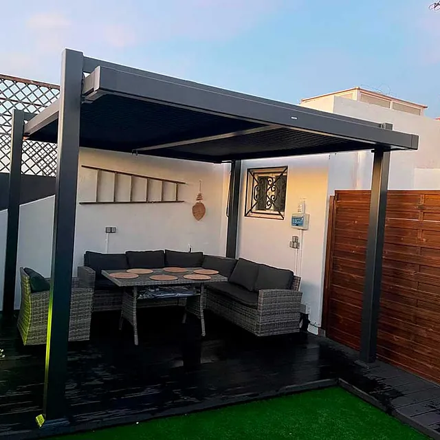 Un patio con sofá, mesa y sillas bajo una pérgola.