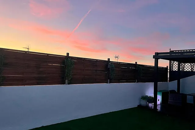 Un patio trasero con una valla de madera y una pérgola al atardecer.
