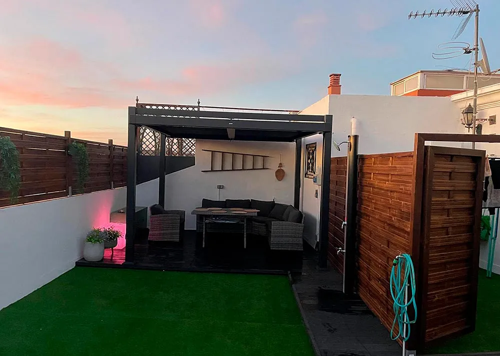 Un patio con pérgola, mesa, sillas y manguera.