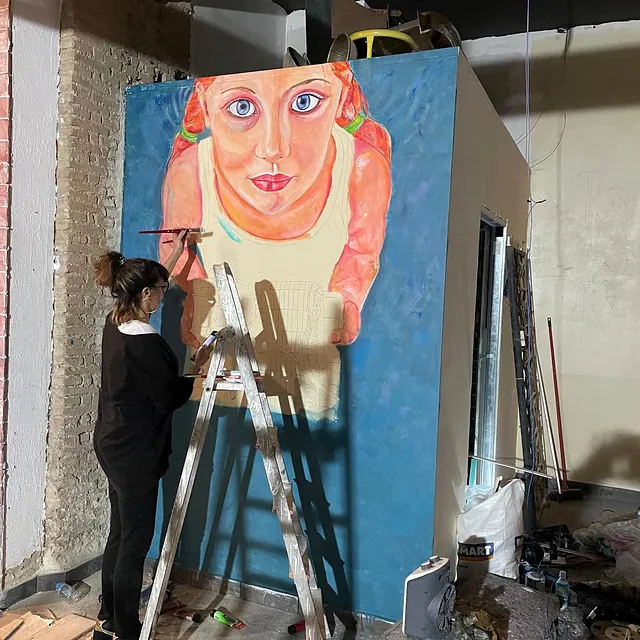 Una mujer está pintando un cuadro de una niña en una pared.