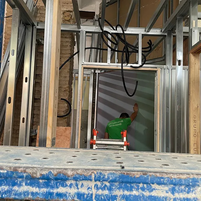 Un hombre con una camisa verde está de pie en una escalera en un edificio en construcción.