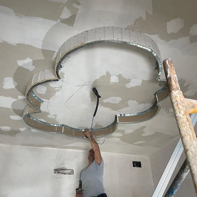 Un hombre está trabajando en el techo de una habitación con una escalera.
