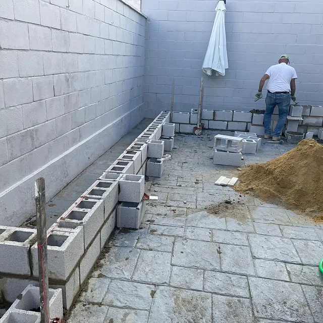 Un hombre con camisa blanca está trabajando en una pared de ladrillos.