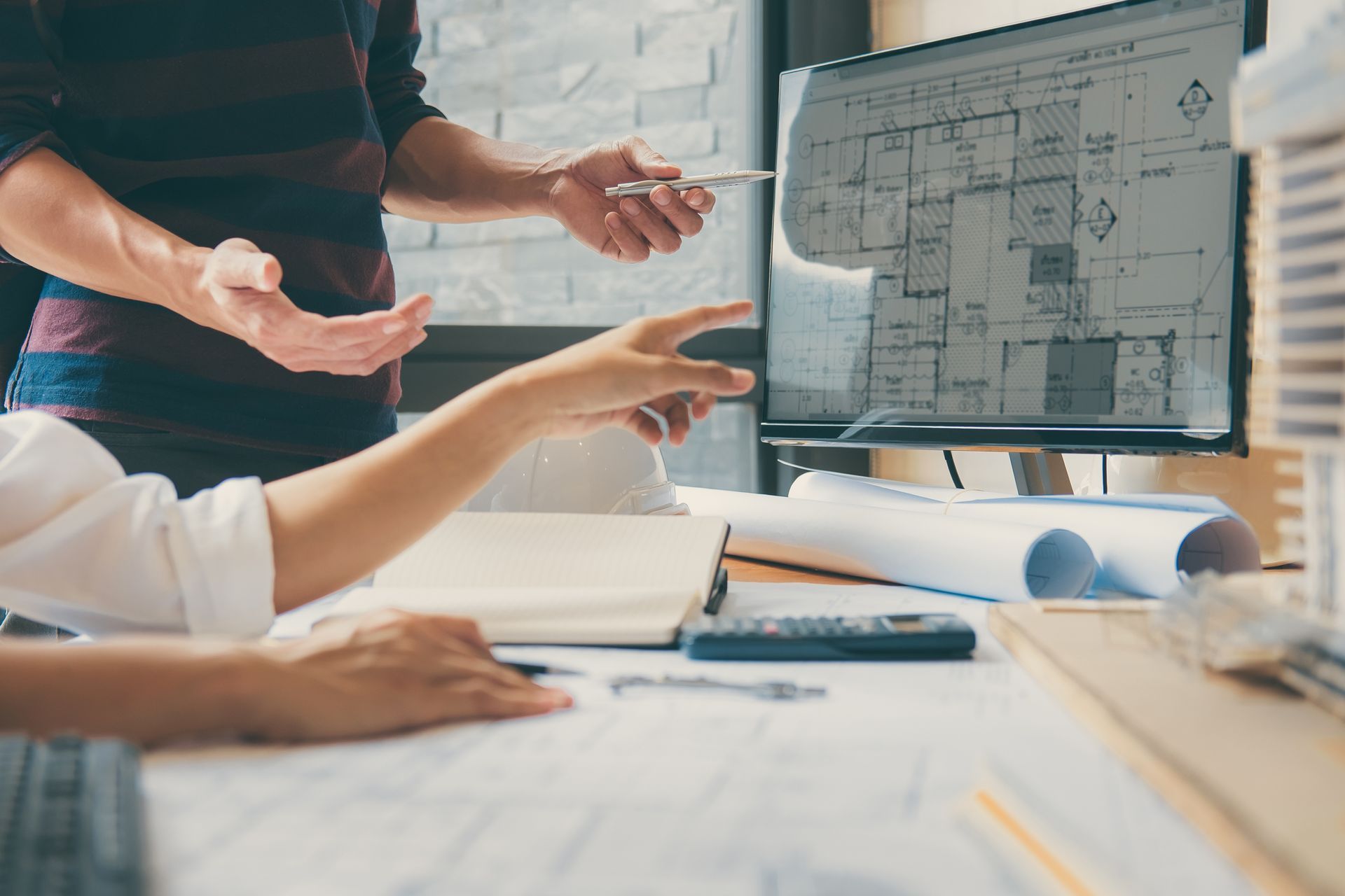 Architekten überprüfen Baupläne auf einem Computerbildschirm, zeigen auf Details und besprechen Projektpläne.