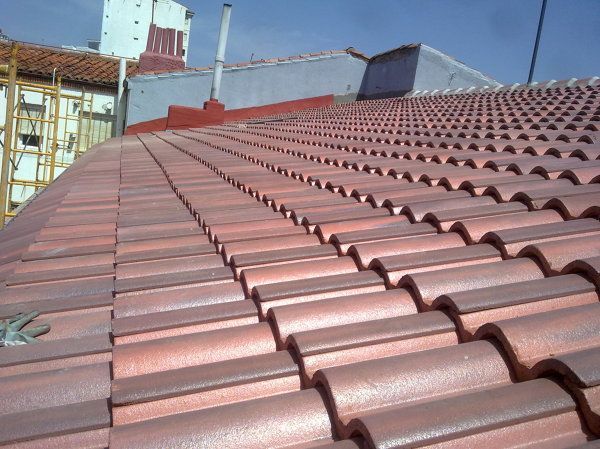 Tejado de tejas rojas de un edificio bajo un cielo azul, con obras visibles al fondo