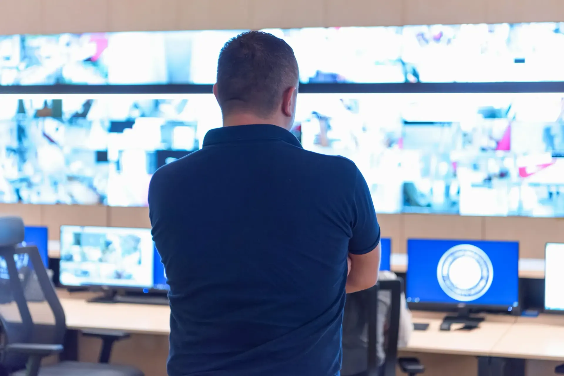 Hombre uniformado en la consola de seguridad, monitoreando pantallas con imágenes de vigilancia.