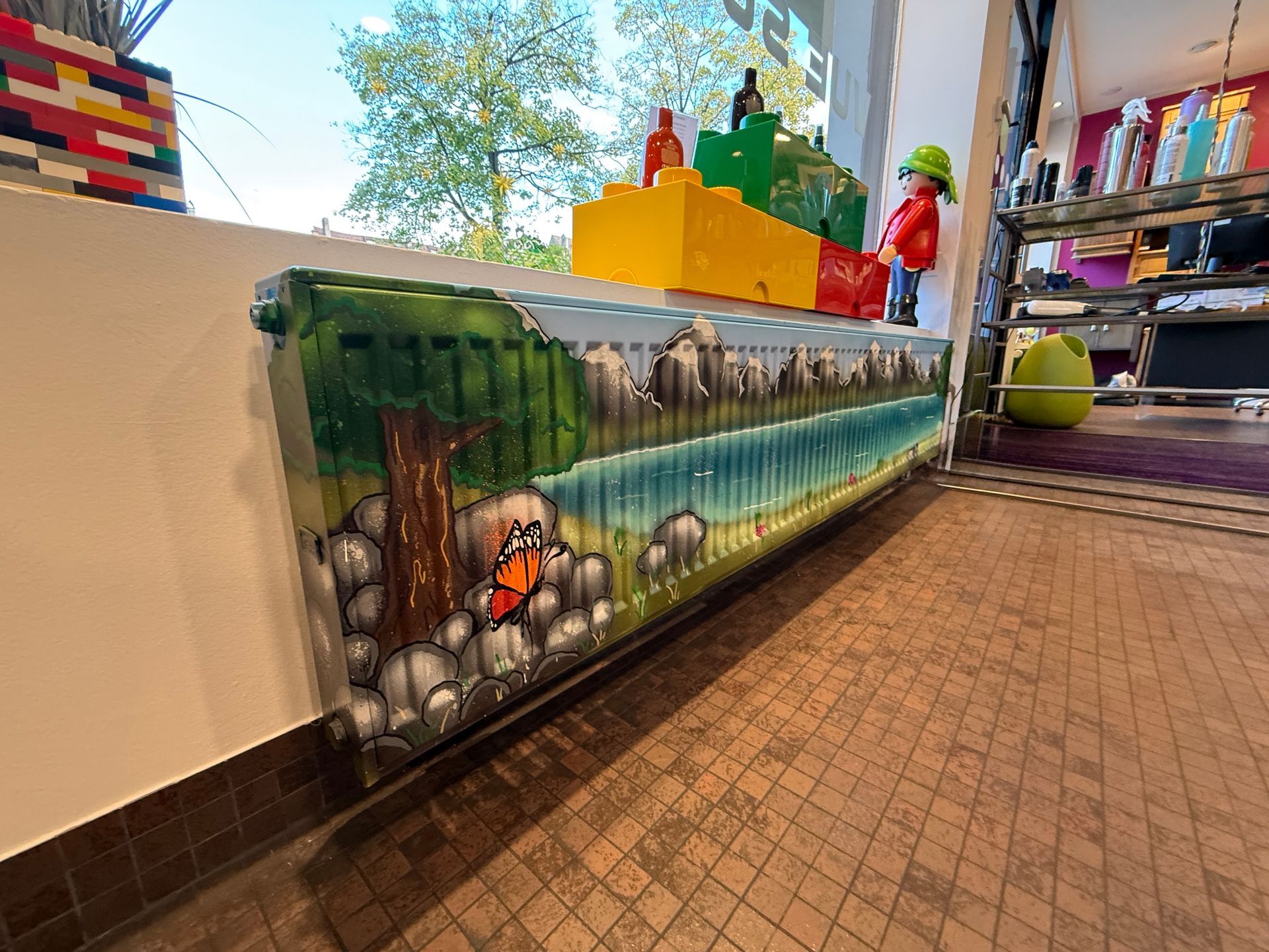 Détail de la peinture d'un radiateur à eau sous une vitrine où des Legos géants et un Playmobil géant sont posés