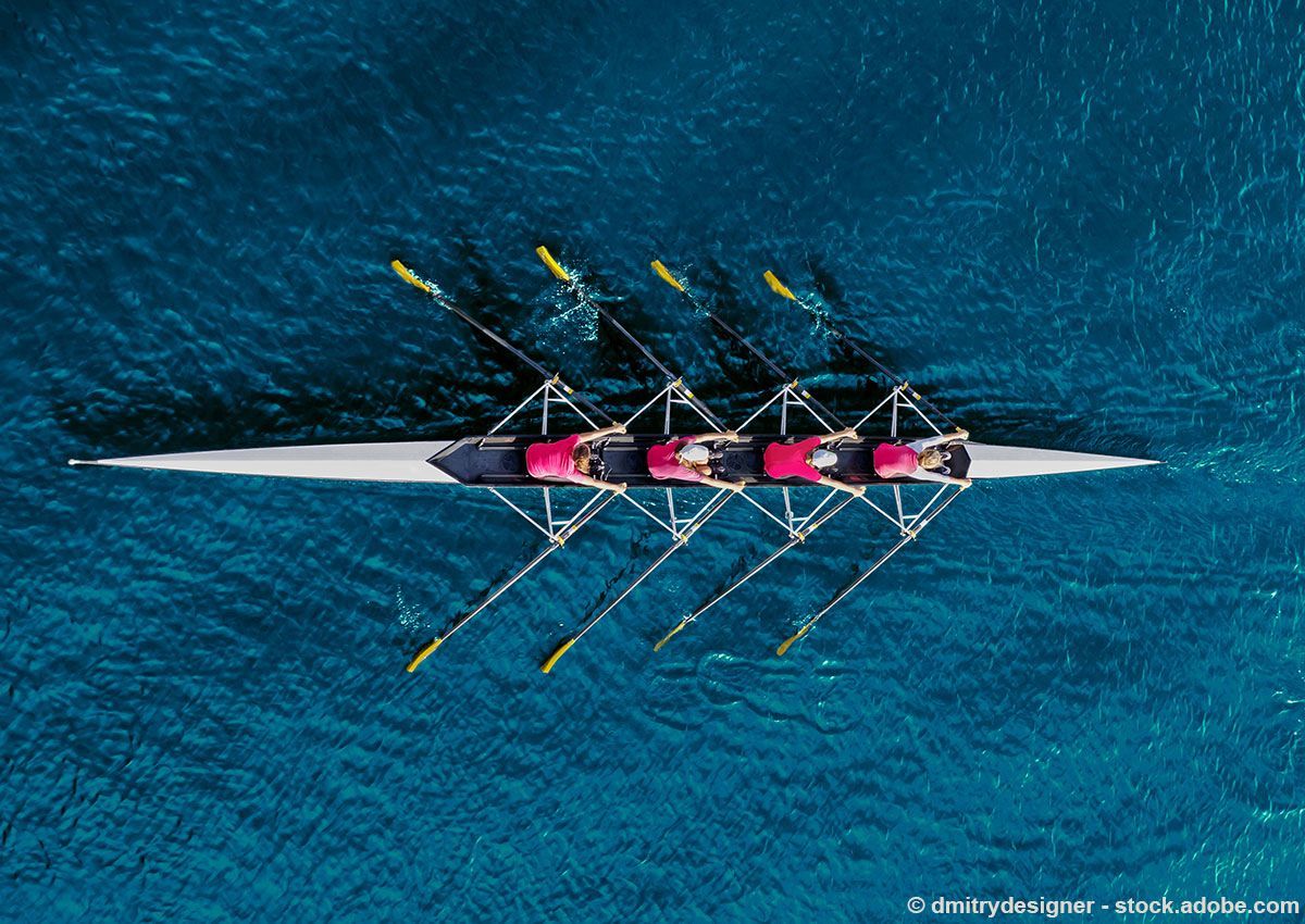 Ruderteam rudert auf blauem Wasser, von oben gesehen.
