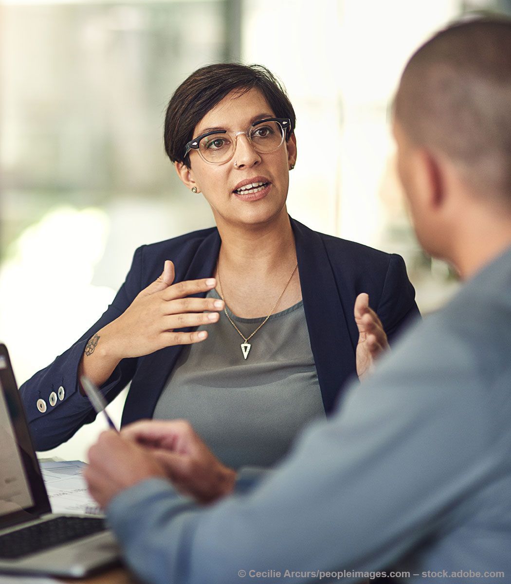 Frau im weißen Hemd schüttelt lächelnd in einem Büro die Hand.