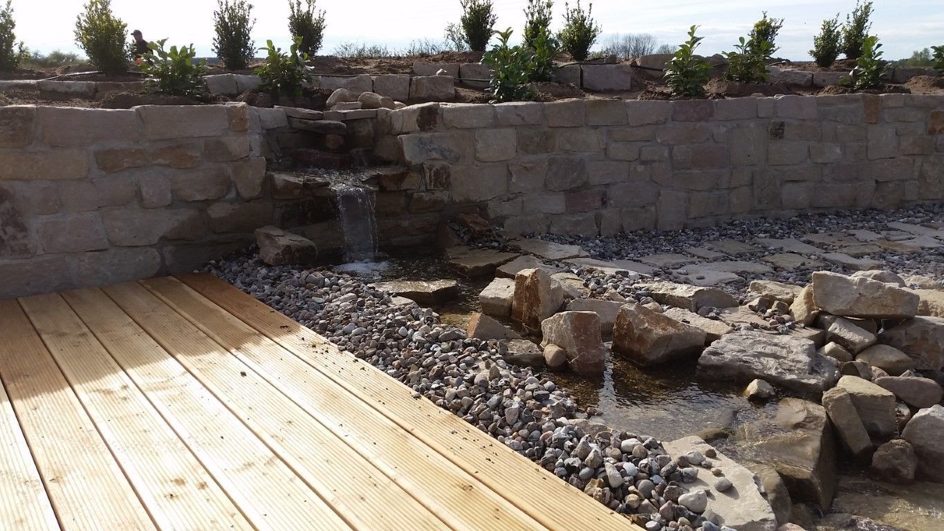 Holzdeck mit Natursteinmauer und Bachlauf