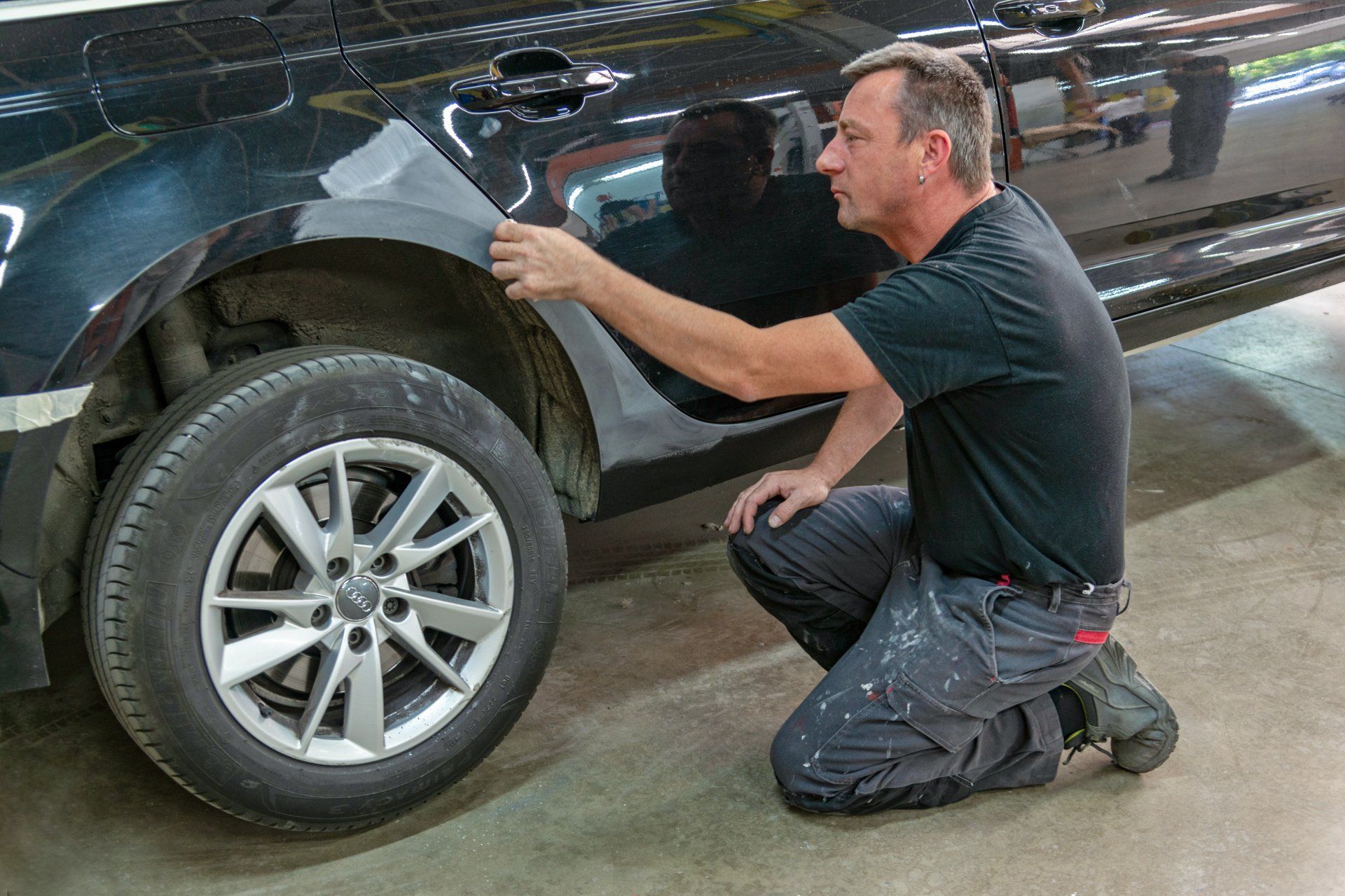 Technicien accroupi devant le flanc droit d'une voiture noire passant un chiffon sur la carrosserie.